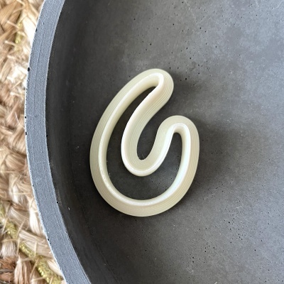 Broche creme em espiral sobre fundo cinza escuro com parte de cesta natural visível