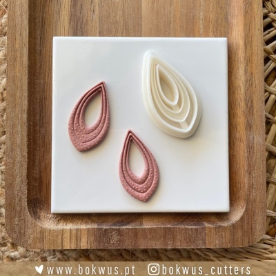 Três cortadores de tecido em forma de gota sobre placa branca num tabuleiro de madeira.