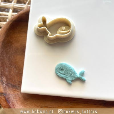 Cortador de massa em forma de baleia e massa azul moldada em forma de baleia sobre prato branco