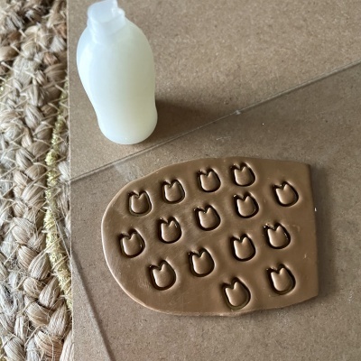 Placa de argila com marcas de cabeça de gato e garrafa branca sobre superfície bege com tapete de fibras