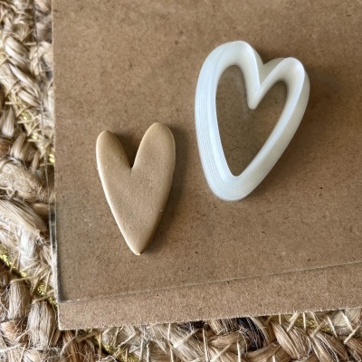 Dois cortadores de coração, um castanho e outro branco oco, sobre cartão e tapete de fibras naturais