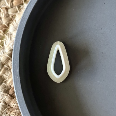 Brinco pendente em acrílico bege e branco em forma de gota numa superfície cinza.