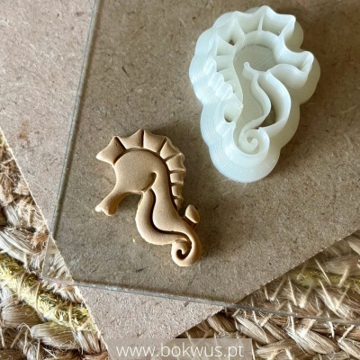 Cortador de massa branco plástico e biscoito cavalo-marinho bege sobre papel castanho e tecido