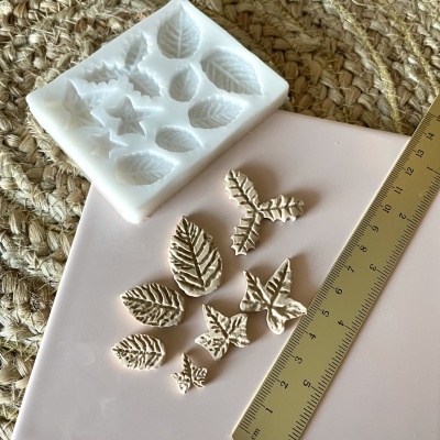 Molde em silicone branco com formas de folhas e estrelas, peças moldadas bege, régua dourada, tapete de palha entrelaçada.