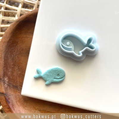 Cortante para bolachas em forma de baleia com bolacha azul claro feita, sobre prato de madeira.