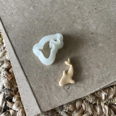 Cortador de massa branco em forma de golfinho com peça de massa bege cortada numa superfície castanha.