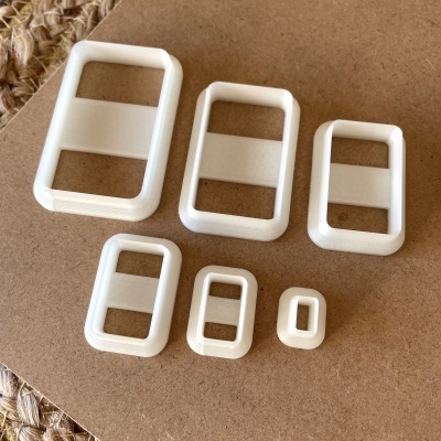 Cinco fivelas de plástico branco retangulares em vários tamanhos sobre superfície castanha