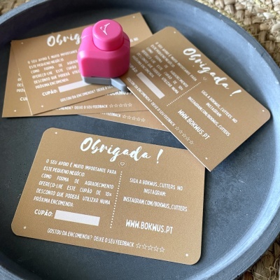 Cartões de agradecimento castanhos com texto branco e um cortador pequeno rosa numa superfície azul.