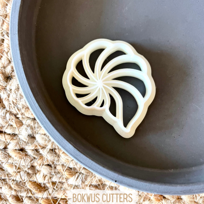 Cortador de massa em forma de concha marinha branco num prato cinza sobre base de palha