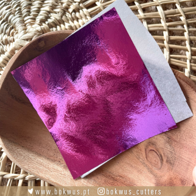 Folha rosa espelhada sobre base de madeira com fundo em tramas naturais