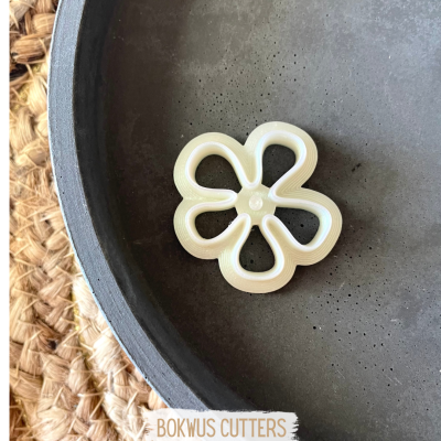Cortador de bolachas em forma de flor branco numa tigela cinzenta sobre tecido trançado