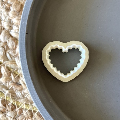Cortador de massa em forma de coração branco sobre prato cinzento com tapete de fibras naturais ao lado