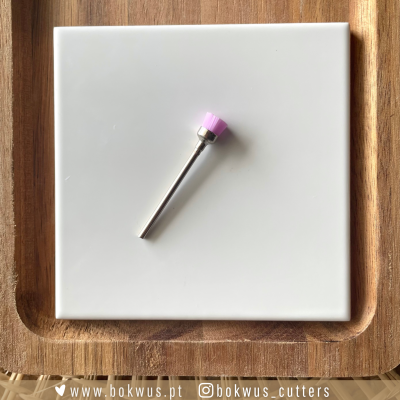 Broca de instrumento rotativo com cerdas rosas em placa branca numa bandeja de madeira