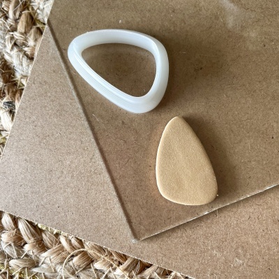 Dois objetos triangulares, um branco e um bege, sobre superfícies de cortiça e plástico transparente.