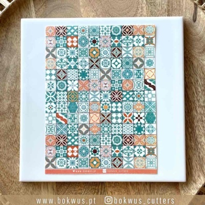 Azulejo quadrado com padrão geométrico colorido sobre superfície de madeira clara.