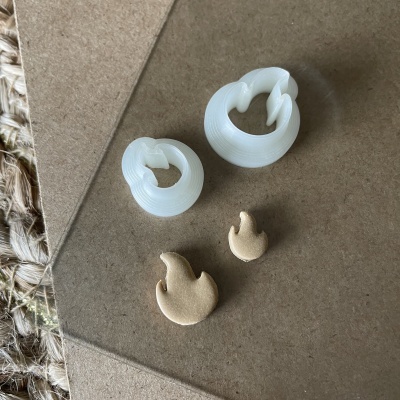 Brincos em acrílico branco e metal dourado em forma de chama sobre superfície castanha