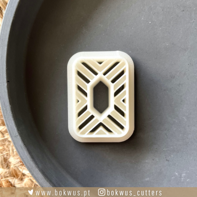 Peça plástica branca com desenho geométrico em fundo cinza fosco.