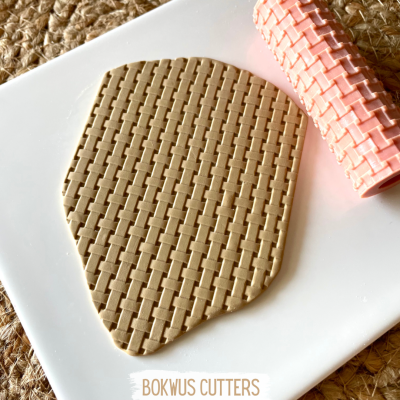 Rolo de massa rosa com padrão quadriculado a estampar massa bege sobre superfície branca