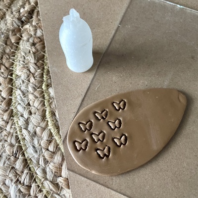 Base plástica branca com relevo de borboletas e massa castanha com padrão de borboletas sobre cartão e ráfia.