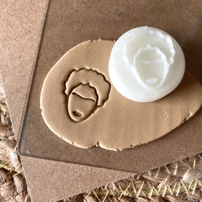 Carimbo branco com rosto estilizado carimbado em massa marrom sobre cartão