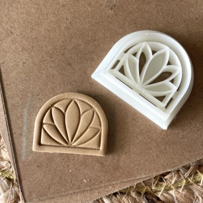 Dois carimbos de silicone ou plástico com padrão de folhas em forma de meia-lua, um branco e um bege, sobre cartão castanho e tecido.