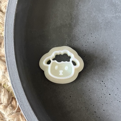 Objeto em formato de ovelha branco e bege dentro de uma tigela cinza escuro