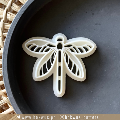 Cortante branco em forma de libélula sobre prato preto próximo de cesta de vime