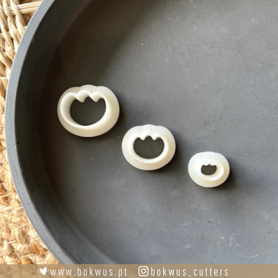 Três cortadores de biscoitos em forma de gato em plástico branco sobre bandeja preta