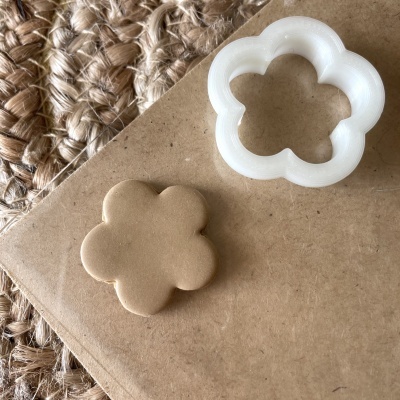 Cortador de bolachas em forma de flor branco e bolacha castanha clara em superfície castanho clara