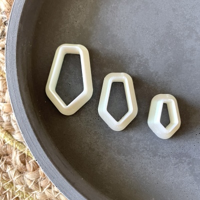 Três moldes brancos geométricos irregulares numa tigela de cerâmica cinzenta escura sobre tapete de fibra natural