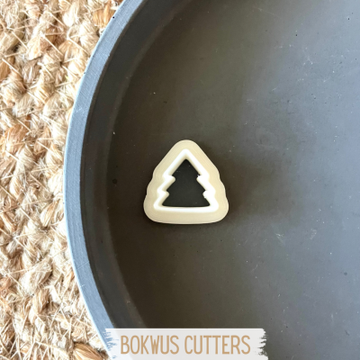 Cortador de bolacha em formato de árvore num prato cinza escuro sobre superfície de fibra natural.