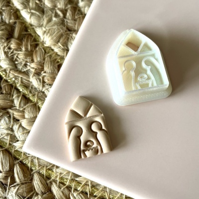 Carimbo de borracha com peça de silicone com desenho de casa e figuras, sobre base rosa clara e fundo entrelaçado