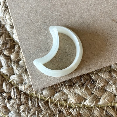 Anel branco em forma de meia-lua sobre cartão e tapete de fibras naturais
