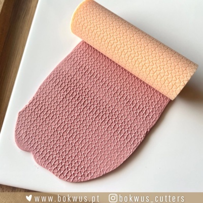 Rolo de massa rosa com textura triangular sobre superfície branca e rolo laranja com padrão semelhante.