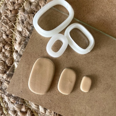 Três moldes plásticos ovais brancos e três peças ovais bege em superfície castanha com tapete fibra natural ao lado.