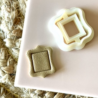 Cortadores de massa branca e peça cortada bege com textura, em superfície rosa clara sobre fundo trançado