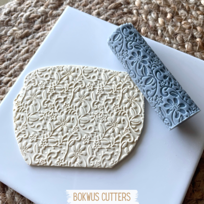 Rolo de textura azul com padrão floral e pasta branca decorada sobre base branca