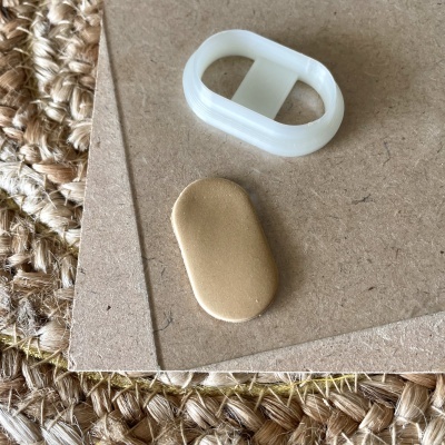 Dois objetos pequenos sobre cartão, um dourado liso e outro branco de plástico com recortes.