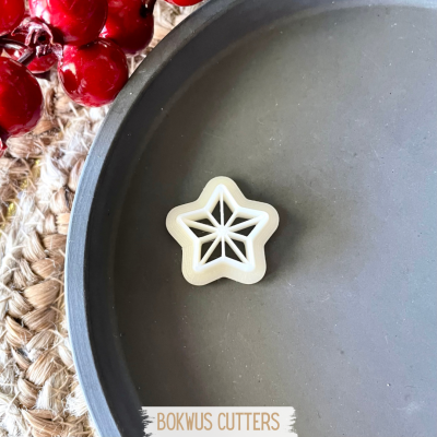 Cortador de bolachas estrela branco num prato cinzento com bagas vermelhas ao lado