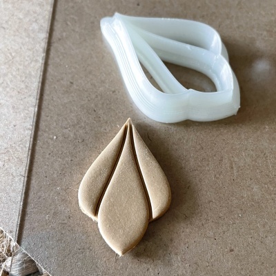 Cortador de massa em plástico branco com forma de pétalas e peça de massa moldada do mesmo formato sobre superfície castanha