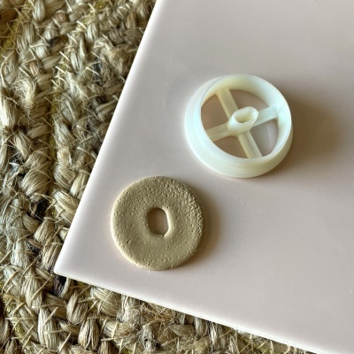 Superfície rosa claro com disco creme e peça plástica branca sobre superfície de corda trançada.