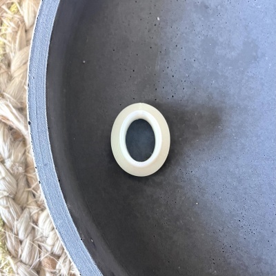 Anel branco com interior transparente numa superfície preta e base de tecido rústico