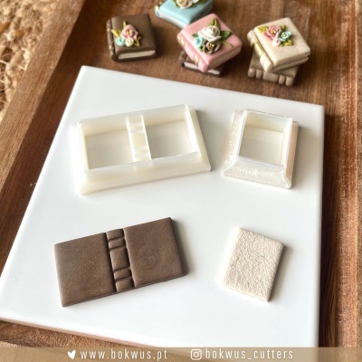 Moldes para pasta americana e pequenos bolos decorados com flores em fundo de madeira.