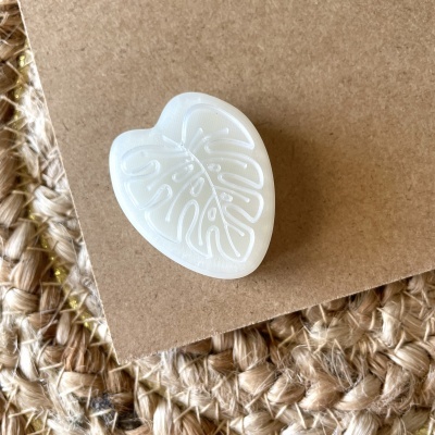 Botão branco em forma de folha em cartão castanho sobre tecido de juta