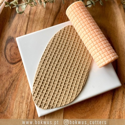 Base quadrada branca com textura de wafer e rolo de massa cor de pêssego com padrão xadrez sobre mesa de madeira