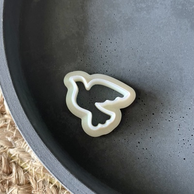 Cortador de plástico branco em forma de pássaro dentro de prato cinzento sobre superfície de fibras naturais