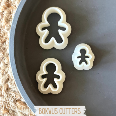 Três cortadores de biscoitos em forma de boneco de plástico branco num prato cinza escuro.