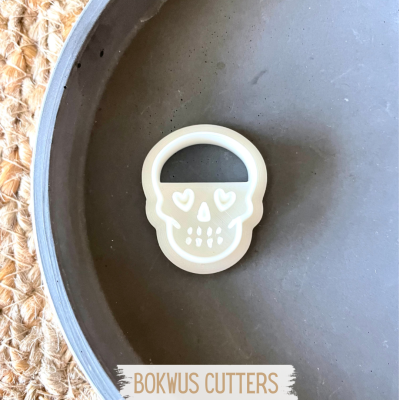 Cortador de biscoito em forma de caveira branca dentro de prato cinza sobre superfície de tecido