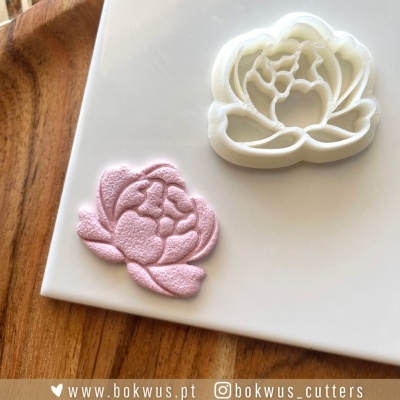 cortador de bolos branco em forma de flor e impressão cor-de-rosa numa placa branca sobre madeira