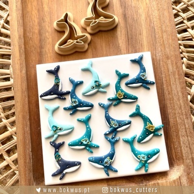 Ímanes ou enfeites em forma de baleia decorados com detalhes florais sobre placa branca e cortadores de massa de baleia em madeira